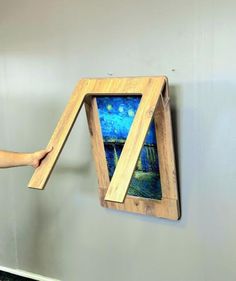 a person is holding up a painting in front of a wall hanging on the wall