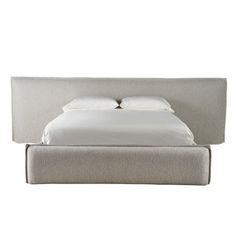 an upholstered bed with two pillows and white linens on the headboard