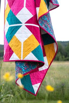 a colorful quilt hanging from a clothes line in a field with wildflowers behind it