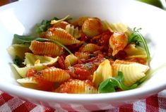 a white bowl filled with pasta and spinach on top of a checkered table cloth