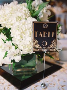 there is a vase with white flowers in it and a table sign on the stand