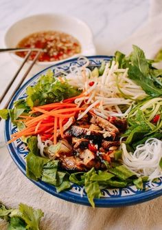 a blue and white plate topped with salad next to a bowl filled with meat, veggies and sauce