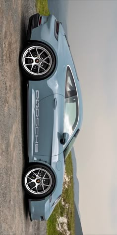 a blue sports car parked on the side of a road next to a body of water