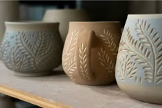 three vases sitting on top of a table next to each other, one with a leaf design