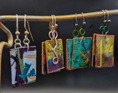 four earrings hanging from a clothes line with metal clips attached to each earring, all in different colors and shapes