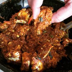 a hand reaching for some food in a skillet