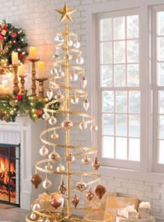 a gold christmas tree with ornaments and lights in front of a fireplace decorated for the holiday season