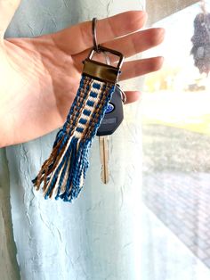 a hand holding a keychain with a blue and white tassel hanging from it