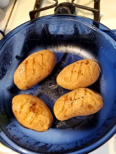 four baked breads in a blue pan on the stove top with water droplets around them