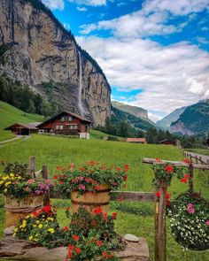 flowers are hanging from the wooden fence in front of a house and mountain with a waterfall