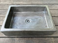 a square metal sink sitting on top of a wooden floor next to a drain faucet