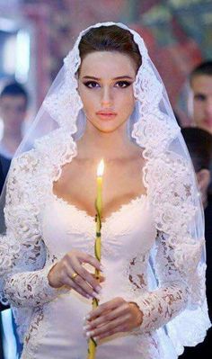 a woman in a wedding dress holding a candle with her hands and looking at the camera