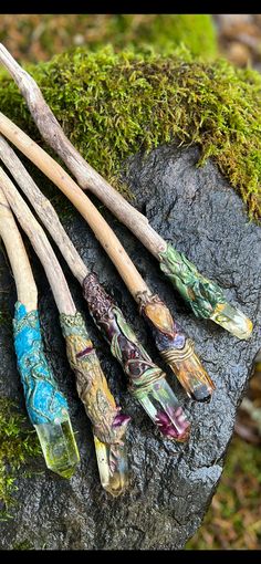 four different colored wooden sticks laying on top of a moss covered rock next to each other