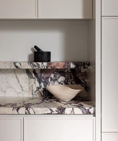 a marble counter top in a kitchen with white cabinets and cupboards, including a bowl