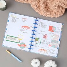 an open planner book next to a candle and some other items on a table with a knitted blanket