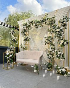 an outdoor wedding setup with white flowers and greenery on the wall, along with candles