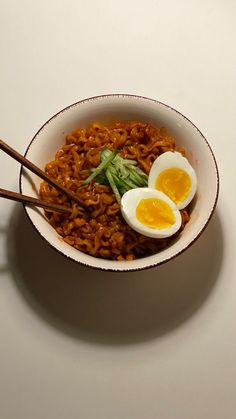 an egg and noodles dish with chopsticks in a bowl on a white surface