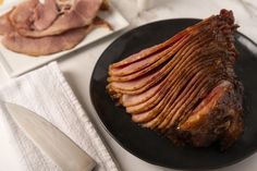 sliced ham on a black plate next to a knife and fork