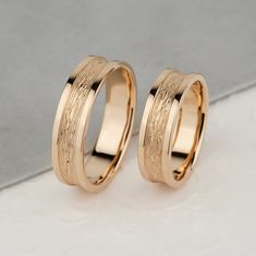 two gold wedding rings sitting next to each other on top of a white countertop