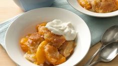 a white bowl filled with fruit and topped with whipped cream next to two spoons