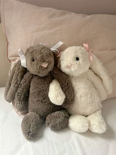 two stuffed animals sitting next to each other on top of a bed near a pillow