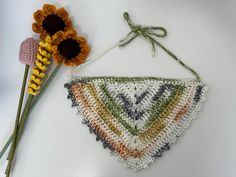 a crocheted triangle hanging from a string next to a flower on a white surface