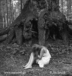 black and white photograph of a woman sitting in front of a large tree trunk with her head down