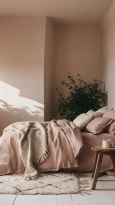 an unmade bed with pink sheets and pillows in a room next to a potted plant