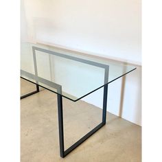 a glass table with metal frame legs on the floor in front of a white wall