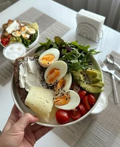 a person is holding a bowl of food with eggs, cheese and tomatoes on it