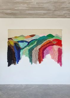 an abstract painting with multicolored fringes hanging on a wall in a white room