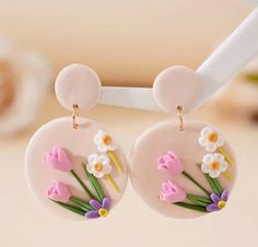 a pair of earrings with flowers painted on them hanging from a hook in front of a table