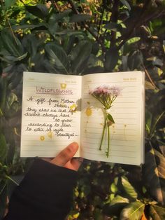 someone holding up a notebook with writing on it and a flower in the middle,