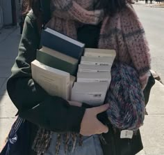 a woman is holding several books in her hands while walking down the street on a cold day