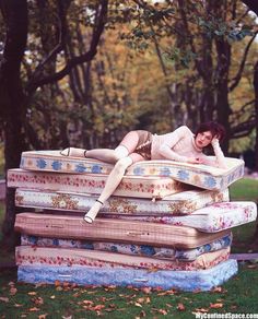 a woman laying on top of several mattresses in the grass with trees behind her