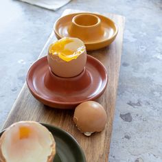 an egg is sitting on a plate next to two plates with one broken and the other half open