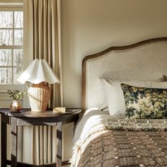 a bedroom with a bed, nightstand and lamp in it's corner next to a window