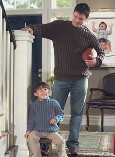 a man holding a football standing next to a little boy on the stairs in a house