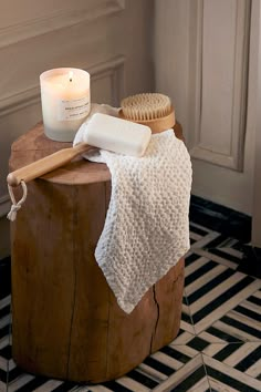 a wooden table topped with a white towel and a brush next to a lit candle