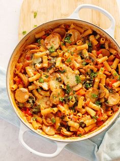 a pot filled with pasta and vegetables on top of a wooden cutting board next to bread