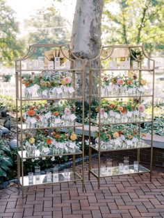 a display case with flowers on it in front of a tree and brick flooring