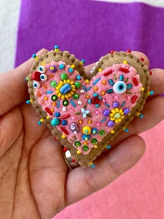 a hand holding a heart shaped cookie with sprinkles and eyes on it