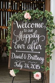 a welcome sign with flowers and greenery on it in front of a barn door