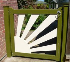 a green and white gate with the sun shining through it's center piece in front of a brick wall