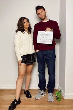 a man and woman standing next to each other in front of a wall holding a sign