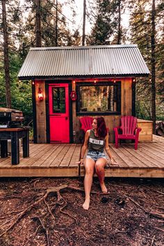 a woman sitting on top of a wooden deck next to a small cabin in the woods