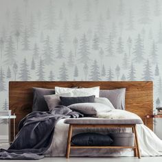 a bed with pillows and blankets on it in front of a wallpapered forest