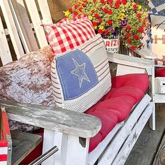 a wooden bench with red and white pillows on top of it next to some flowers