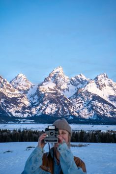 a person holding up a camera in front of snow covered mountains