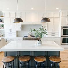 a kitchen island with three stools in front of it and two lights hanging over the top